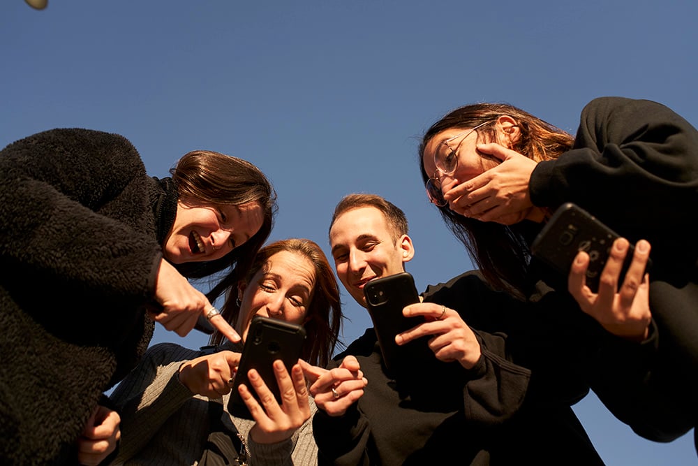 Low-angle of a group of friends using a smartphone and and laugh